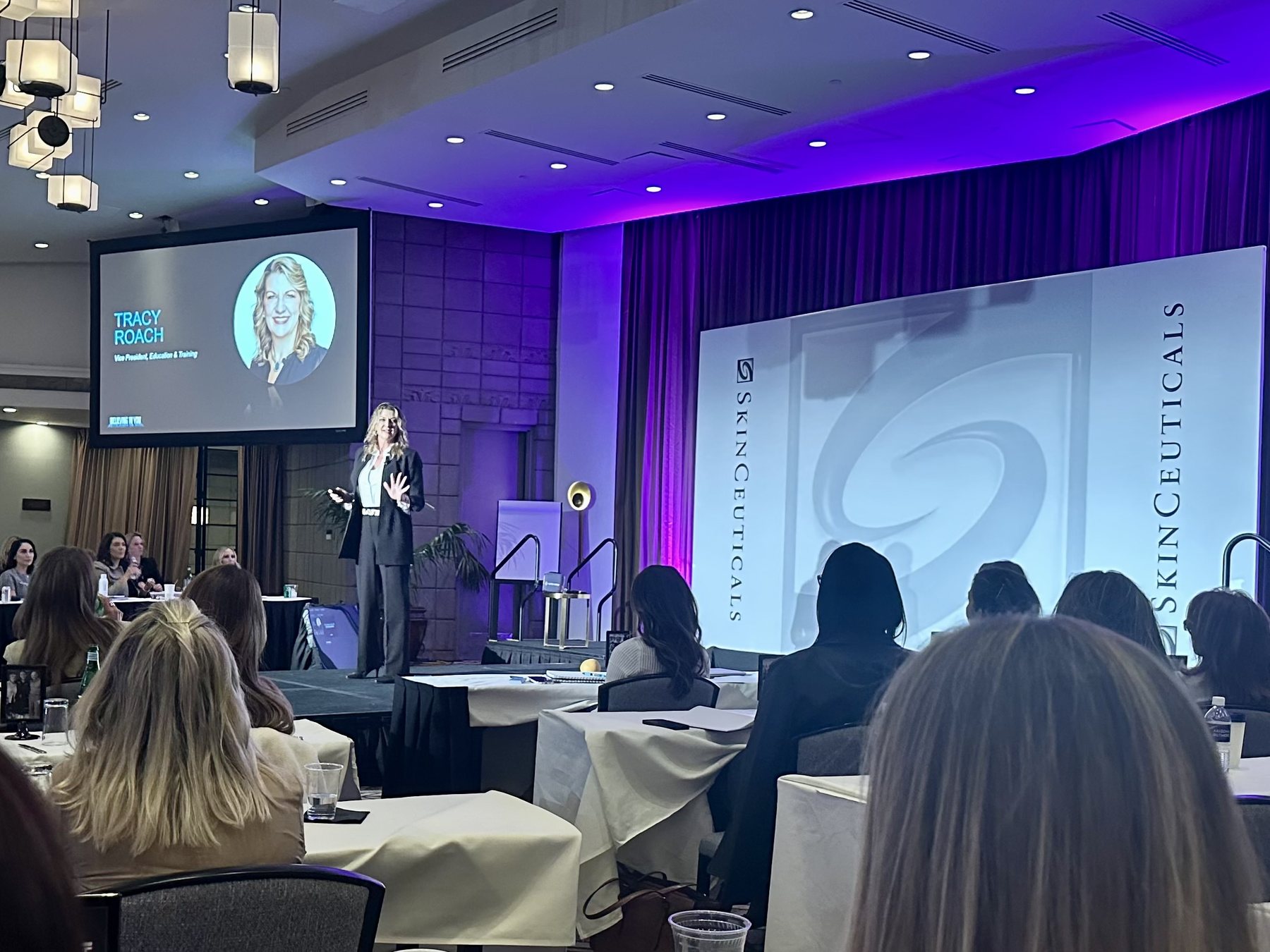 Tracy Roach presenting on stage at an aesthetics training event